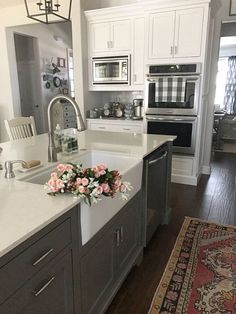 a white kitchen with gray cabinets and pink flowers on the sink countertop in front of an oven