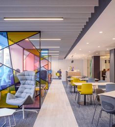 the interior of an office with colorful chairs and tables in front of glass partitions