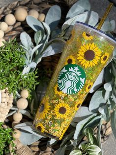 a starbucks cup with sunflowers on it sitting in the middle of some plants