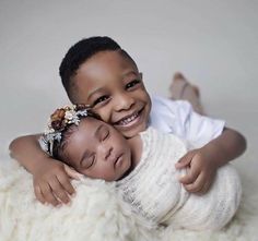 two young children cuddling each other on a fluffy white blanket and smiling at the camera