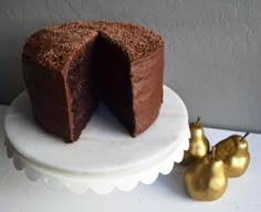 a chocolate cake sitting on top of a white plate next to two gold pears