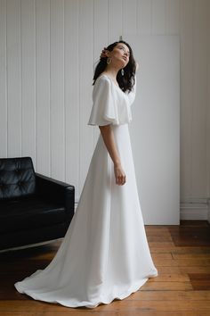 a woman in a white dress standing on a wooden floor next to a black chair