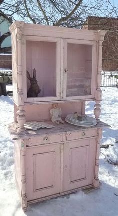 an old pink china cabinet sitting in the snow