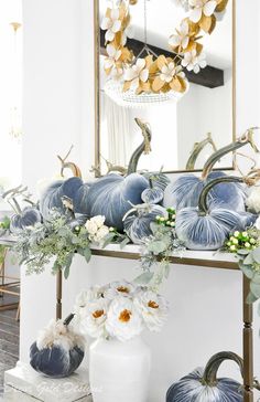 a white vase filled with flowers and pumpkins on top of a table next to a mirror