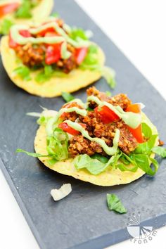 three tacos with meat, lettuce and tomatoes on a slate platter