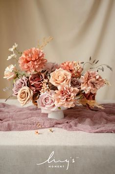 a vase filled with lots of pink flowers on top of a white cloth covered table