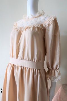 Beautiful True Vintage dress from the late 1970s or early 1980s. Synthetic fabric. Relatively high neck, semi transparent decollete with ruffled bib, half long slightly puffed sleeves with elasticated cuffs. Lace decorated decollete, cuffs and skirt. Sewn on tie belt for a cute large bow on the back. Zipper in the back. Lined skirt. Looks great with a pair of tan 70s mid block heel shoes. BRAND: Lacella ERA: 1970s, 1980s COLOR: Apricot with white lace decorations Fabric: No fabric tag, but it`s Puffed Sleeves Dress Vintage, Beige Feminine Vintage Dress For Party, Beige Vintage Dress For Party, Feminine Beige Vintage Dress With Ruffles, Beige Vintage Dress With Lace Trim, Vintage Beige Prairie Dress With Ruffles, Fitted Beige Prairie Dress With Ruffles, Vintage Cream Prairie Dress With Ruffles, Feminine Vintage Cream Dress With Lace Trim