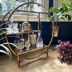 a shelf with glasses and bottles on it next to a potted plant in front of a window