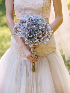 a woman in a wedding dress holding a bouquet of blue and white flowers on her arm