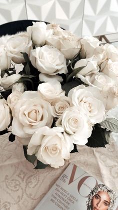 a bouquet of white roses sitting on top of a table next to a magazine cover