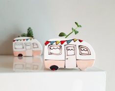 two ceramic campers with plants growing out of the front and back doors, on top of a white surface