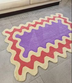 a purple and red rug on the floor in a living room with a couch behind it