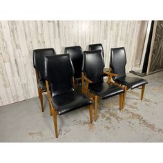 a set of four black leather dining chairs with wooden legs and back rests against a wood paneled wall