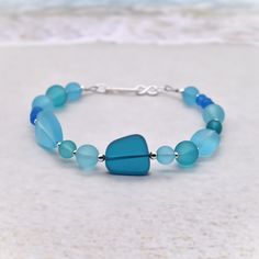 This is a beautiful sea glass bracelet with sterling silver accent beads and a sterling silver infinity clasp. The sea glass beads are recycled glass that have been cultured and gently frosted to resemble glass that has been tumbled in the sea and sand for years.  The colors range from soft aqua to  to a deep Pacific blue.  The shapes are varied and range from 4 mm rondels, 6, and 8 mm round beads to larger nuggets.  The accent beads are sterling silver 2 mm, 2.5 mm, and 3 mm.  The closure is a sterling silver hook that goes into an infinity ring. The bracelet is 7 inches and will fit most.  If you would like a different size, please message me and I will be happy to make one for you! Will arrive in an organza gift bag.  Wonderful and unique gift. All components are .925 sterling silver. Adjustable Blue Jewelry With Recycled Glass, Adjustable Blue Jewelry Made Of Recycled Glass, Adjustable Blue Recycled Glass Jewelry, Blue Czech Glass Bracelets For Beach, Blue Czech Glass Bracelet For Beach, Blue Czech Glass Beach Bracelet, Blue Czech Glass Beach Jewelry, Blue Glass Beaded Bracelets For Beach, Recycled Bracelets