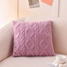 a pink pillow sitting on top of a couch next to a cup and saucer