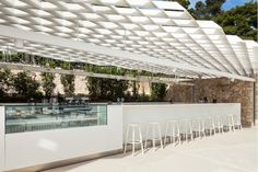 an outdoor bar with white chairs under a pergolated roof