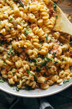 a white bowl filled with pasta and parsley on top of a black cloth next to a wooden spoon