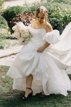 a woman in a white dress is walking through the grass with her wedding gown on