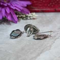 "This beautiful piece is handcrafted with exquisite detailing and features a genuine mottled blue-grey Agate stone that measures 1.5\" long and almost 1\" at its widest point. This measurement includes the solid sterling setting with its studded and gently curved ribbon-like design. The band fits a US size 10 finger and cannot be re-sized as the stone is already set (though you may order a custom ring). This ring is one of a kind and has matching earrings to go with it. The earrings measure 1.25 Unique Agate Jewelry With Matching Earrings, Oval Matching Earrings For Collectibles, Collectible Oval Matching Earrings, Adjustable Moss Agate Gemstone Jewelry, Silver Agate Jewelry With Matching Earrings, Artisan Jewelry With Matching Earrings For Collectors, Nickel-free Oval Agate Jewelry, Handmade Silver Moss Agate Jewelry, Artisan Collectible Jewelry With Matching Earrings