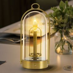 a glass and metal lantern sitting on top of a table next to a wine glass