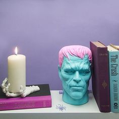 two books and a candle on a table next to a busturine with pink hair