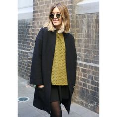 a woman in black coat and yellow top standing on sidewalk with brick wall behind her