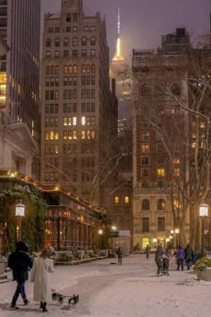 people are walking in the snow near tall buildings and street lamps at night with lights on