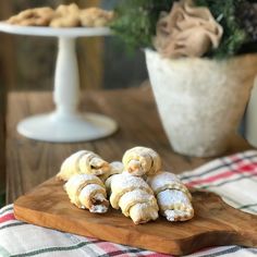 several pastries on a wooden cutting board next to a potted plant and table cloth