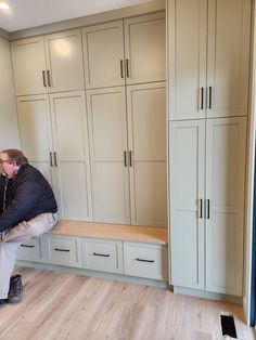 a man sitting on top of a wooden bench in a room filled with cupboards