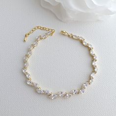 a gold bracelet with crystal beads and a rose on the side, next to it is a white flower