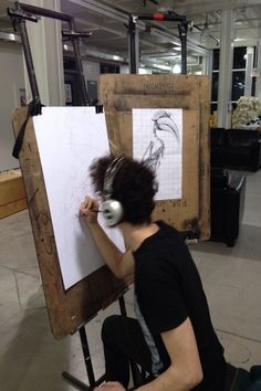 a man sitting in front of an easel with headphones on his ears and writing on a piece of paper