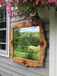 a mirror hanging on the side of a house with pink flowers in front of it