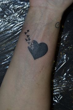 a heart shaped tattoo on the wrist with birds flying out of it's center