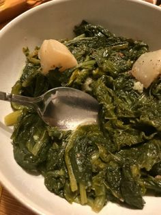 a white bowl filled with spinach and other food on top of a wooden table