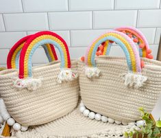 two straw bags with rainbow handles and pom - poms on the bottom one has a tassel