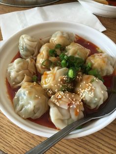 a white bowl filled with dumplings covered in sauce and garnished with green onions