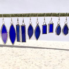 blue glass and silver earrings hanging from a tree branch on the beach with sand in the background