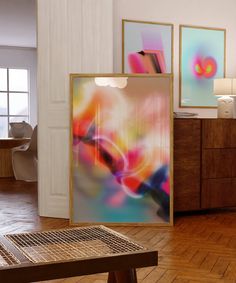 an abstract painting is on display in a room with wood floors and white walls, along with a wooden coffee table