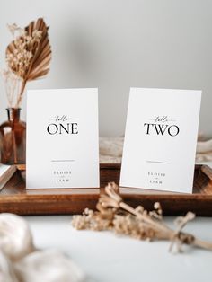 two place cards sitting on top of a wooden tray with dried flowers in the background