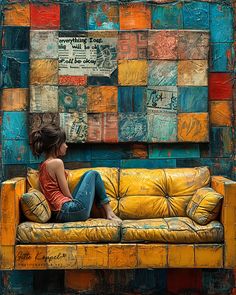 a woman sitting on top of a yellow couch in front of a colorful brick wall