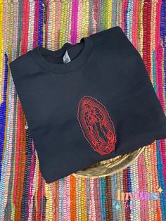 Virgencita Embroidered Crewneck Sweatshirts! All Sweatshirts are a 50% cotton, 50% polyester blend.Sizes offered are S-3XL. ALL SWEATSHIRTS ARE UNISEX.Are slightly oversized.THIS IS ONLY AVALIABLE IN LIGHT PINK, BLACK, TAN OR LIGHT GRAY SWEATERS 🖤All designs will be embroidered with the colors seen in the image. However due to the nature of embroidery some will have small imperfections.Our current processing time is 1-2 weeks due to the high volume of website and sales platforms orders. Order m Black Long Sleeve Embroidered T-shirt, Black Embroidered Logo T-shirt For Fall, Black T-shirt With Embroidered Logo For Fall, Black Long Sleeve Top With Custom Embroidery, Black T-shirt With Custom Embroidery For Fall, Black Crew Top With Custom Embroidery, Embroidered Black T-shirt For Fall, Black Crew Neck Top With Custom Embroidery, Black Embroidered Text Sweatshirt Crew Neck