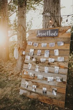 a wooden sign with photos pinned to it in front of some trees and string lights