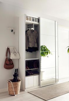 an open closet with clothes hanging on the door and a basket in front of it