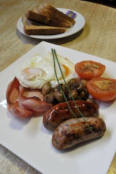 a plate with sausages, tomatoes, eggs and toast on it next to two slices of bread