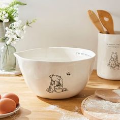 a white bowl sitting on top of a wooden table next to eggs and utensils