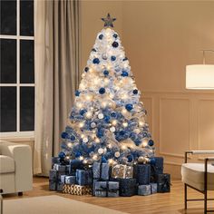 a blue and white christmas tree in a living room with presents on the floor next to it