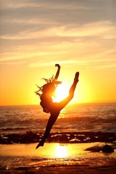 a woman doing a handstand on the beach at sunset