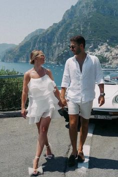 a man and woman walking next to a white car on the side of a road