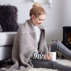 a woman sitting on the floor holding a coffee cup and wearing a knitted sweater