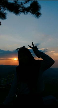 a woman making the peace sign with her fingers in front of an orange and blue sky